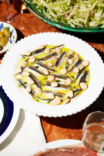 A plate of white anchovies in olive oil topped with marcona almonds, marjoram and orange zest.CreditPaul Quitoriano